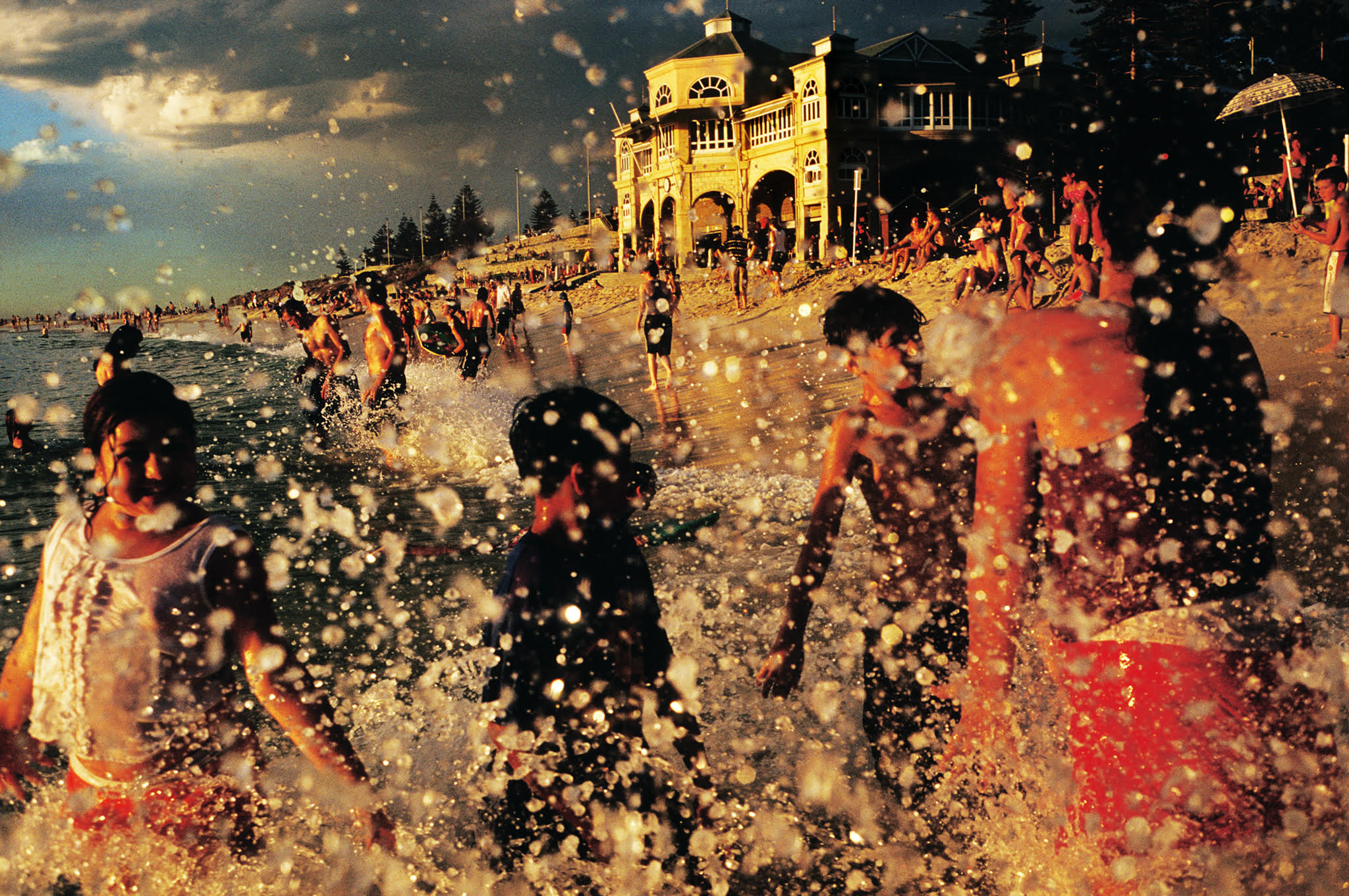 Photograph by Narelle Autio of blurred figures splashing in the waves, with Perth beach in the background