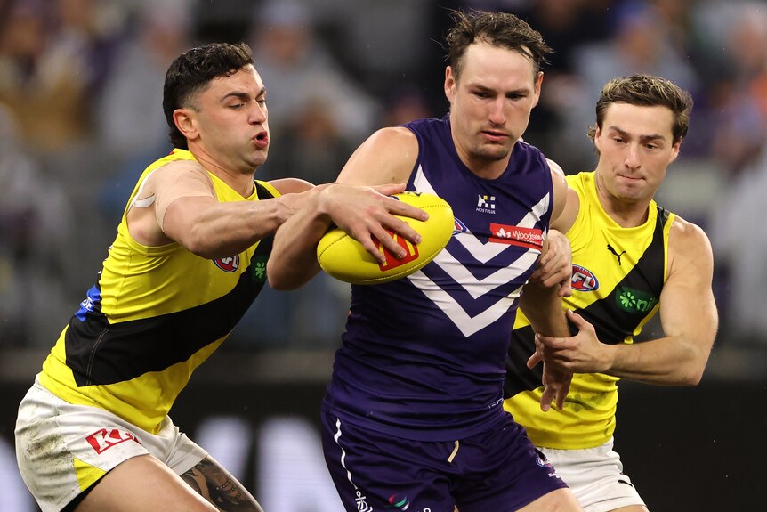 Brennan Cox holds the ball for the Dockers as two Richmond opponents attempt a tackle.