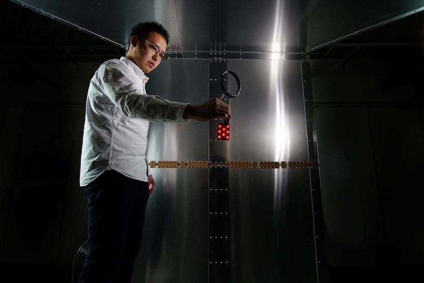 A man inside a room with metal walls holds a device shaped in a coil