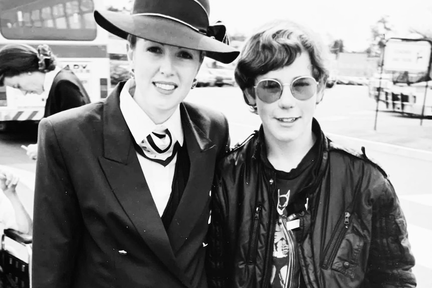 Black and white photo of Lou and a boy smiling, Lou in flight attendant uniform and hat, boy wearing sunglasses and jacket.