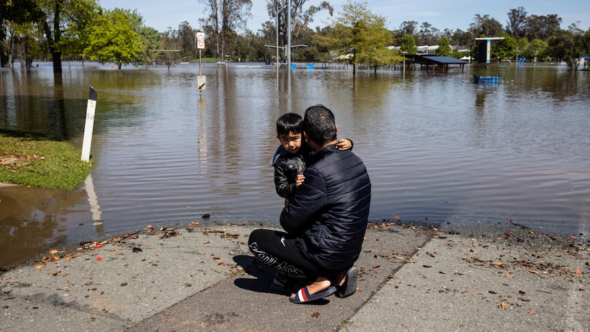 A man hugs his young son in front of a flooded street.
