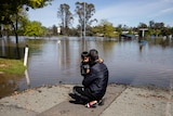 A man hugs his young son in front of a flooded street.