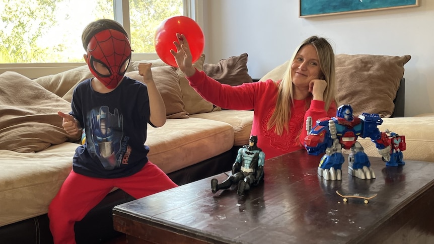 A mother and child dressed as a superhero sit next to each other with toys. 