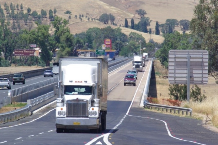 Trucks and cars travelling along a road, with rolling country hills in the background.