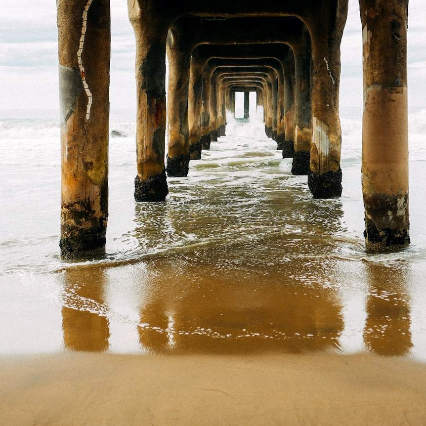 Woman walks towards pier on the edge of a sea.