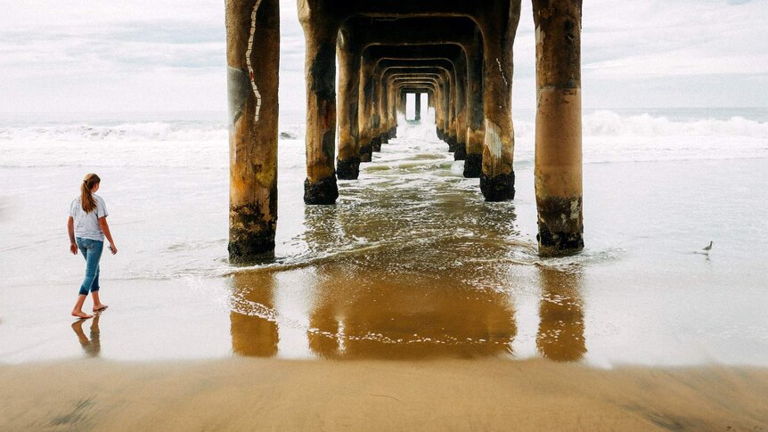 Woman walks towards pier on the edge of a sea.