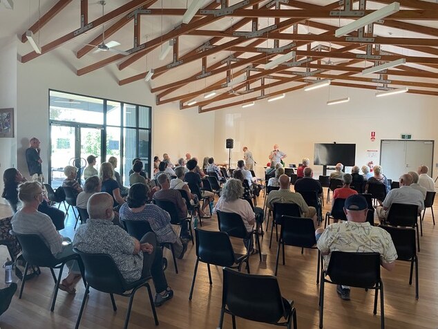 A group of people sit on chairs in a community hall. 