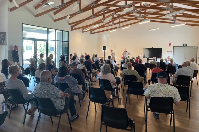 A group of people sit on chairs in a community hall. 