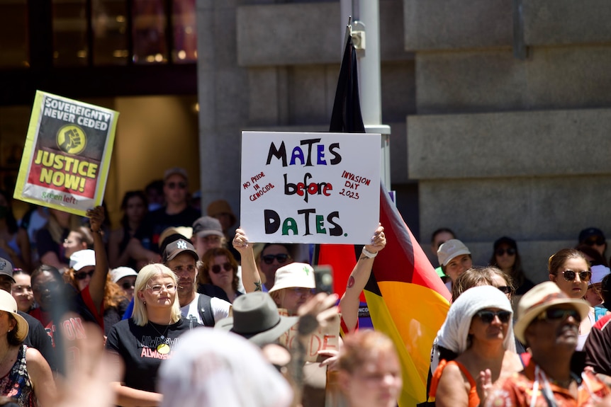 A person holds up a sign stating 'mates before dates' in a crowd of people