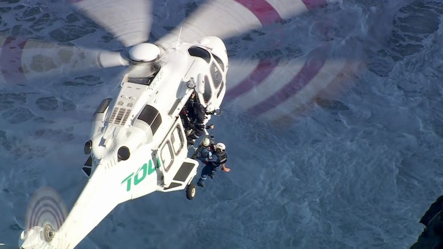 A birds-eye view of a helicopter flying over water with motion blurs from the blades. 