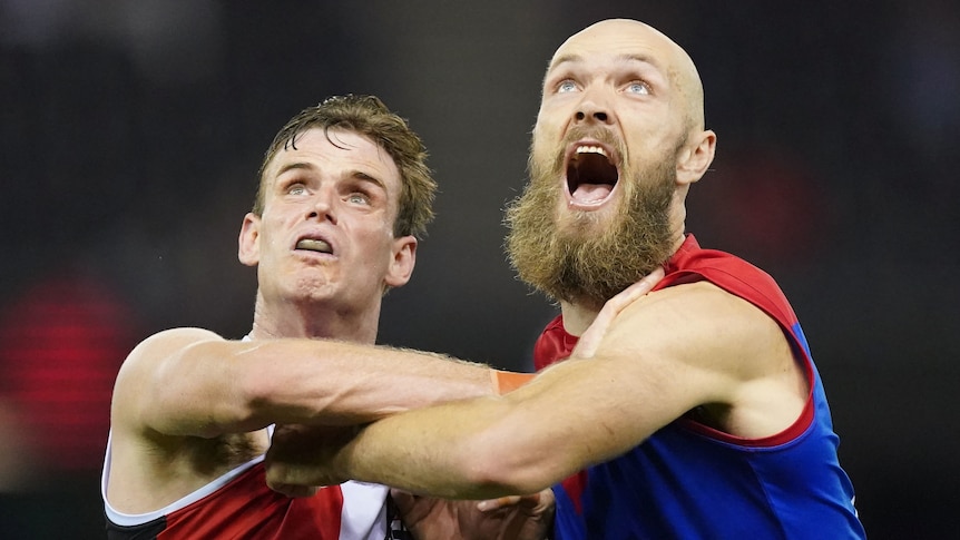 A St Kilda AFL player leans against a Melbourne opponent as they prepare to contest the ball.