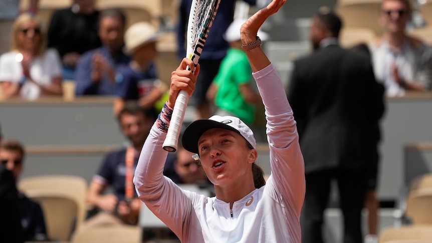 Poland's Iga Świątek applauds the crowd clapping her racquet above her head after a win at the French Open.