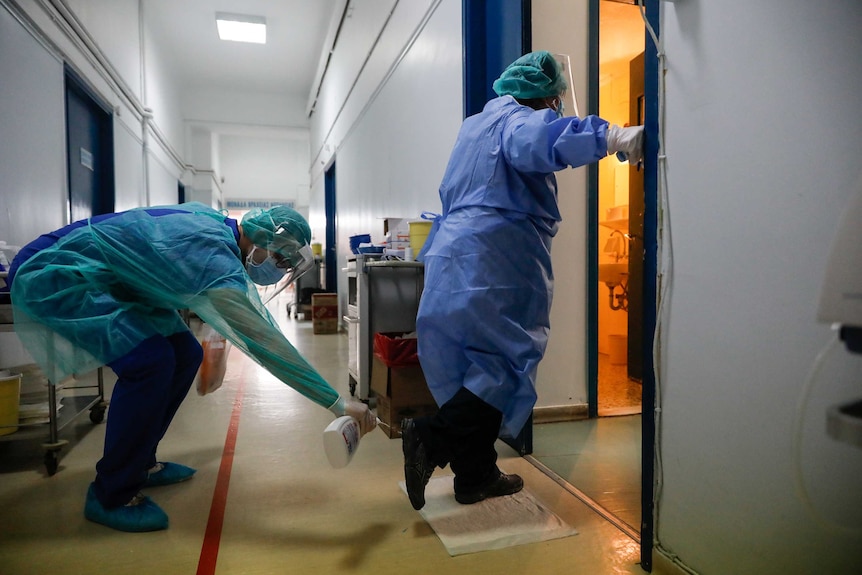 Doctors in full PPE, with one spraying disinfectant on the other doctor's feet.