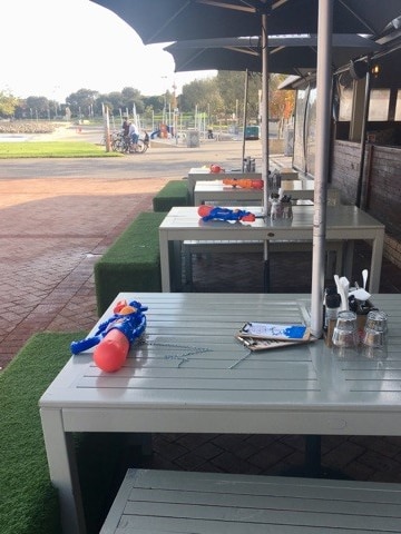 A line of outdoor cafe tables with blue and red water guns on them.