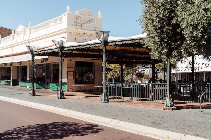 The cafe's outdoor dining area is empty, tables are out but there are no chairs.