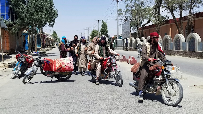A group of men dresses in Afghan clothing with guns on an empty city street.