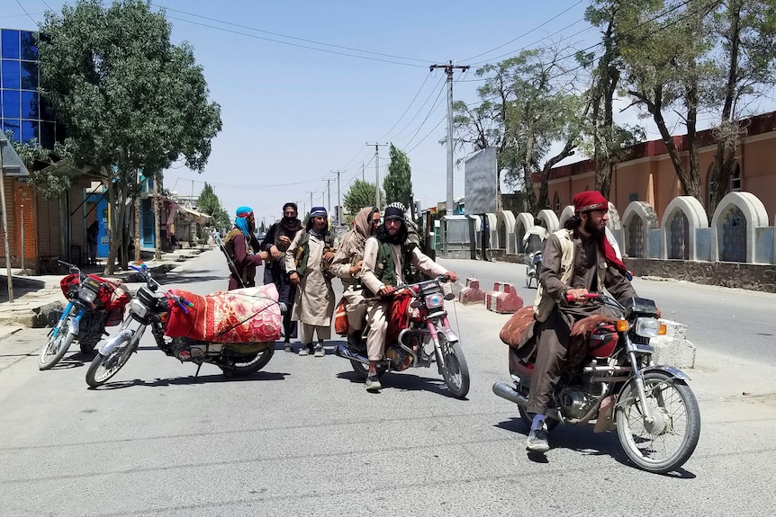 A group of men dresses in Afghan clothing with guns on an empty city street.