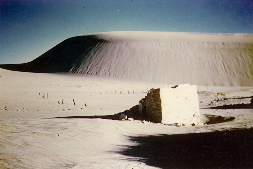 The top of a chimney protrudes from a sand dune.