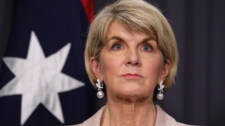 Julie Bishop looks out into the middle distance while standing in front of an Australian flag.