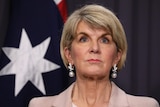 Julie Bishop looks out into the middle distance while standing in front of an Australian flag.