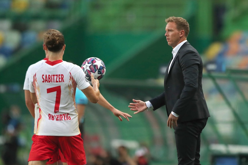 Julian Nagelsmann, wearing a dark suit, throws the ball to a member of his team