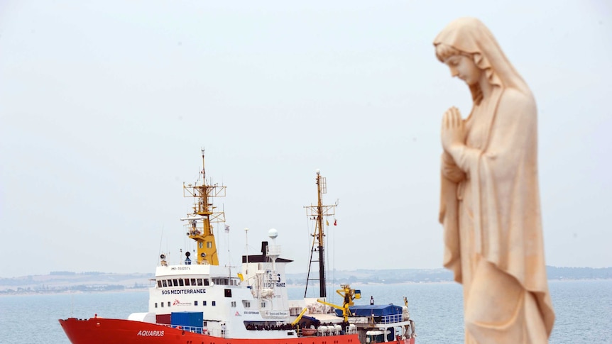 A praying statue sits in the foreground as the Aquarius boat sails in the background