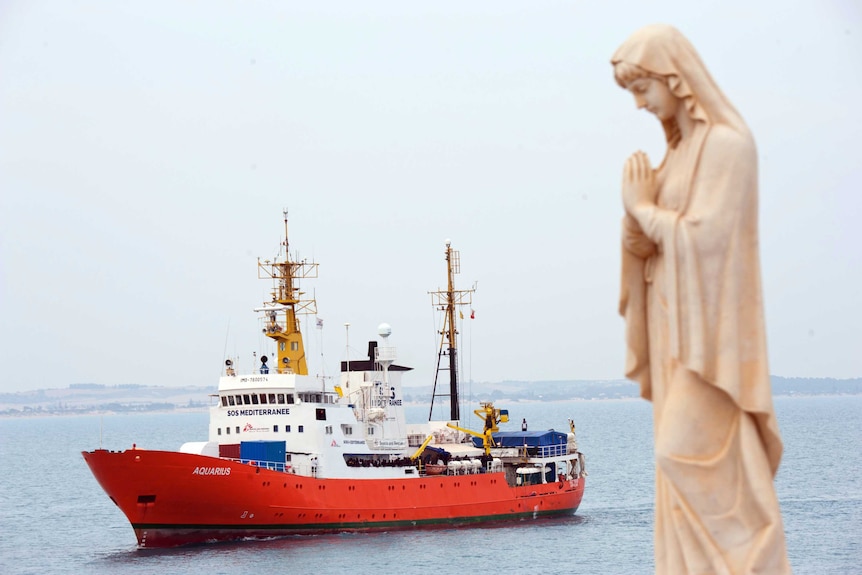 A praying statue sits in the foreground as the Aquarius boat sails in the background