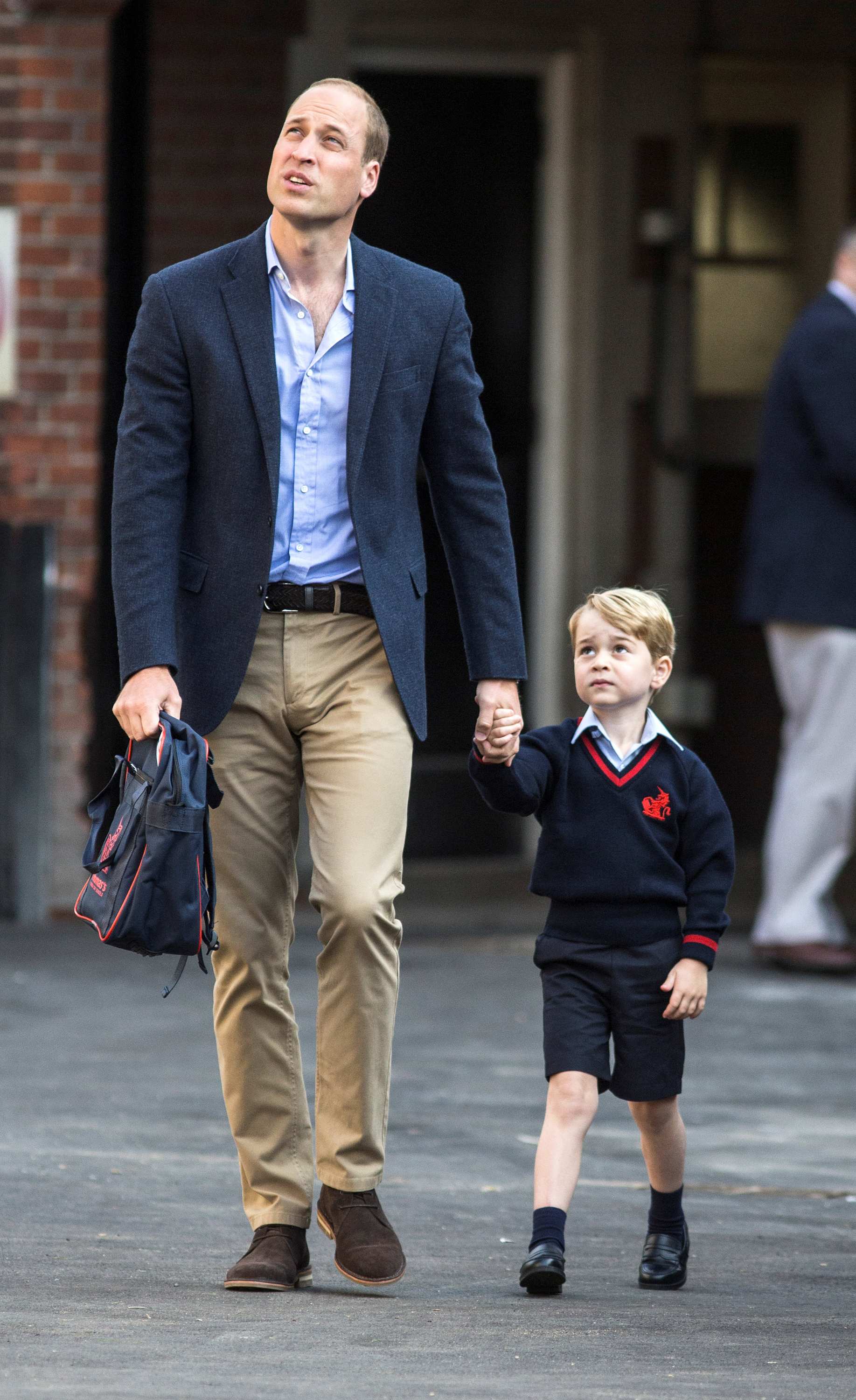 Prince William carries a school bag as he walks hand in hand with Prince George.