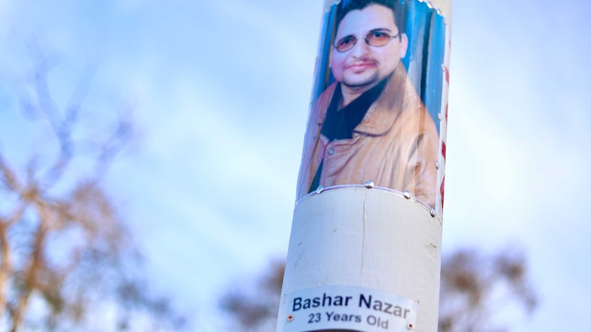 A photo of a young man and a homemade plaque pushed into a white pole using thumbtacks.