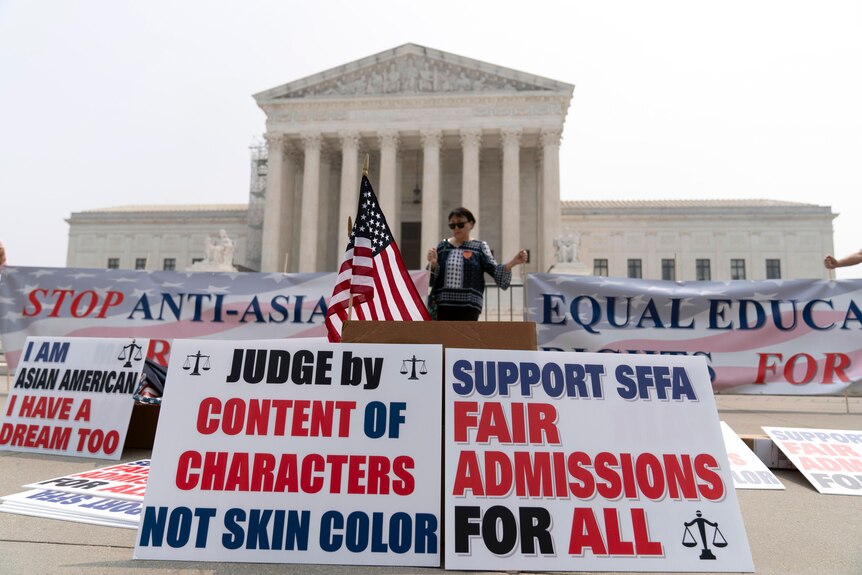 A person protests outside of the Supreme Court in Washington with banners in the front.