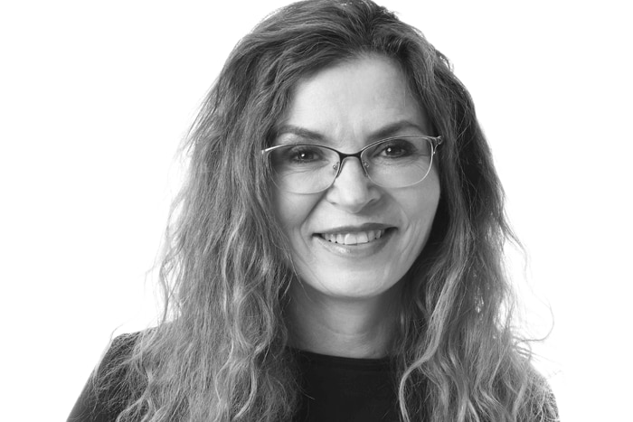 A black and white photo of Dee Madigan wearing glasses and with long hair and a black top