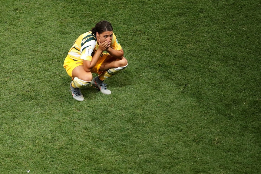 Sam Kerr crouching down with her hands over her mouth.