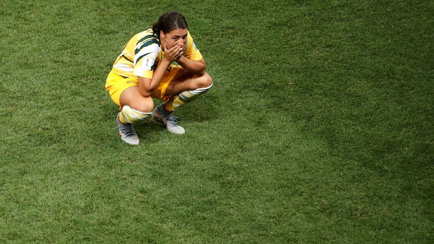 Sam Kerr crouching down with her hands over her mouth.