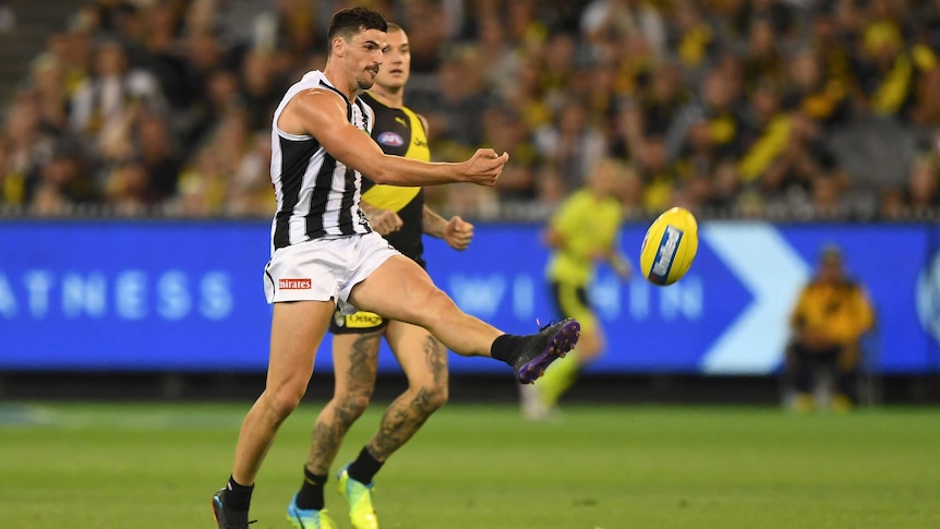 An AFL player kicks the ball in the midfield, as an opponent fails to get close enough to stop him.