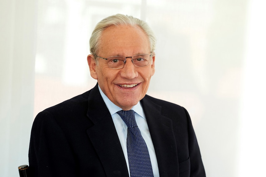 An older man in a black suit jacket with a blue shirt and tie.