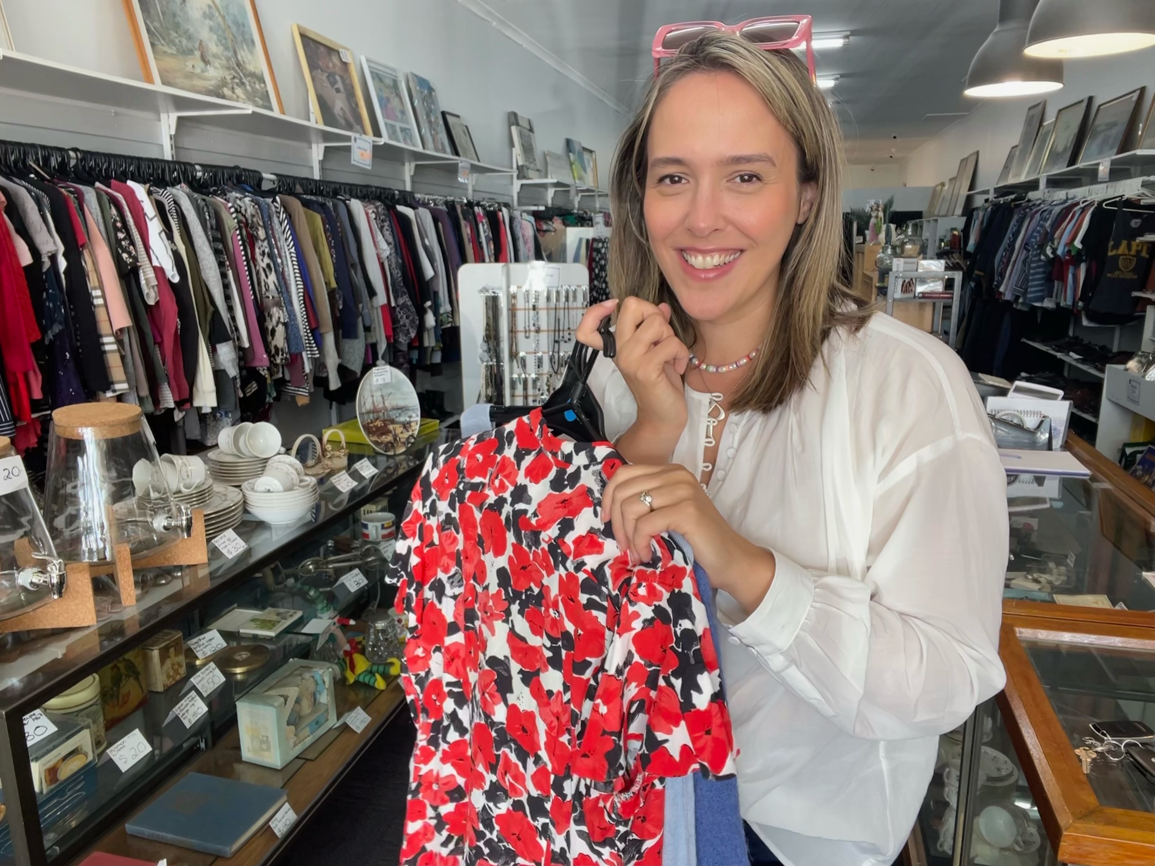Naarm/Melbourne based Bec Brewin poses inside an op shop holding a selection of clothes, she posts her finds on TikTok.