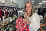 Naarm/Melbourne based Bec Brewin poses inside an op shop holding a selection of clothes, she posts her finds on TikTok.