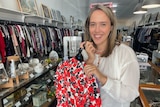 Naarm/Melbourne based Bec Brewin poses inside an op shop holding a selection of clothes, she posts her finds on TikTok.