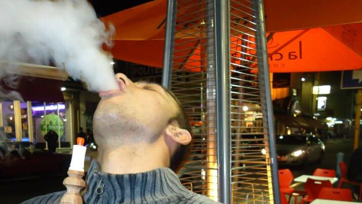A man using a hookah pipe exhales shisha smoke.