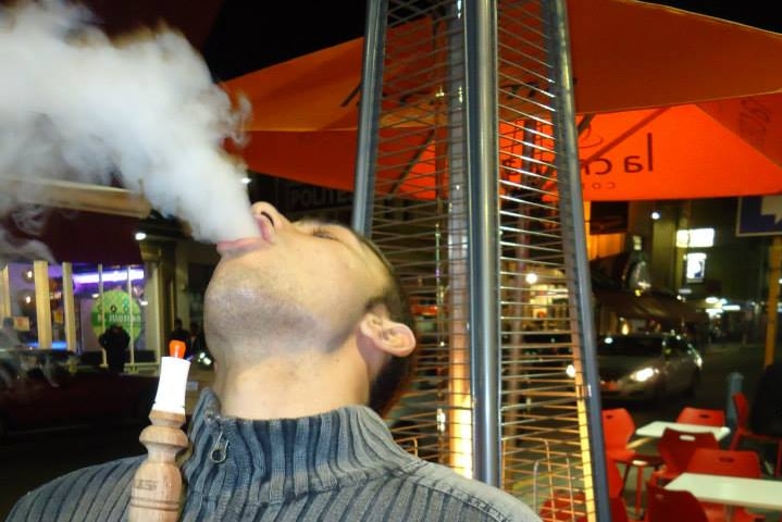 A man using a hookah pipe exhales shisha smoke.