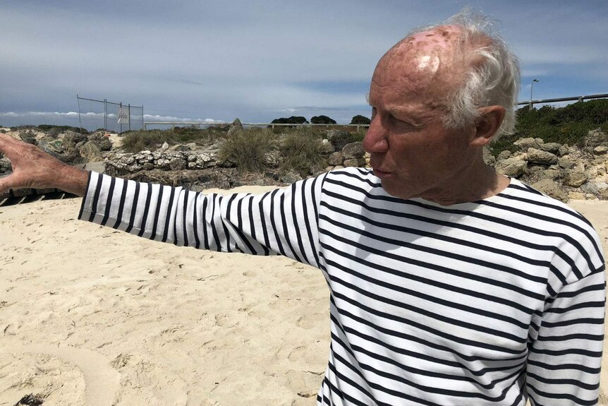Mature man in striped shirt stands on beach and points out to sea
