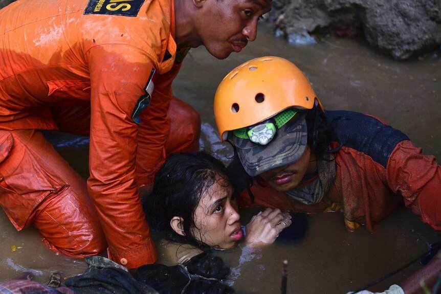 A woman being pulled out of murky water by rescue workers