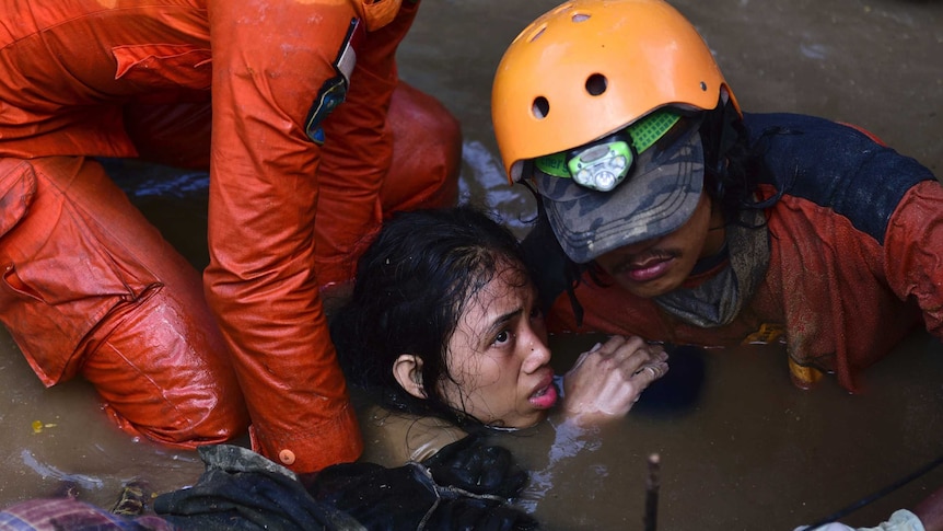 A woman being pulled out of murky water by rescue workers