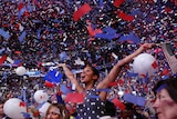 A woman in a polka dot dress waves an American flag as confetti and balloons fall around her