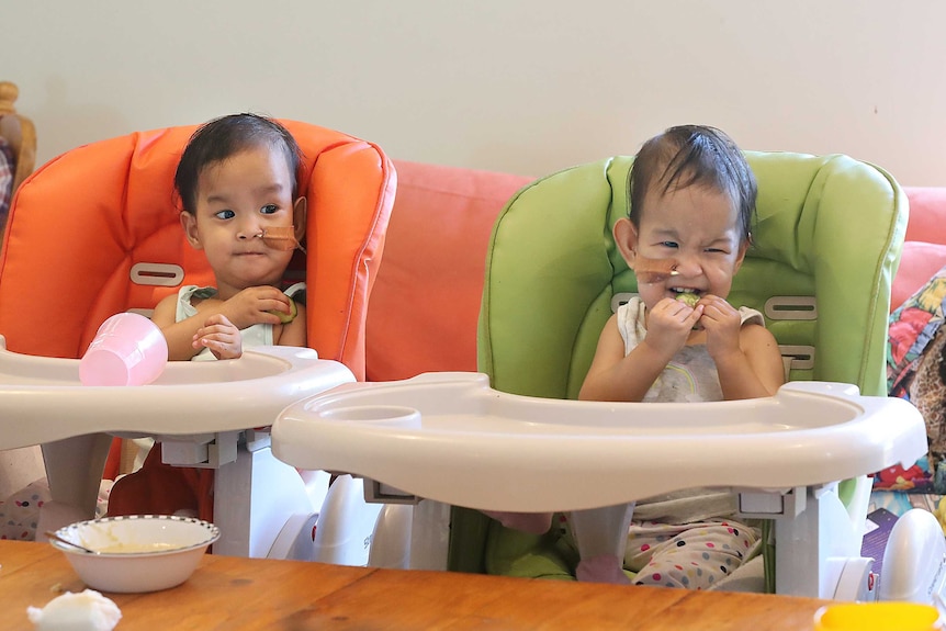 Twin girls sitting in matching high chairs eating food