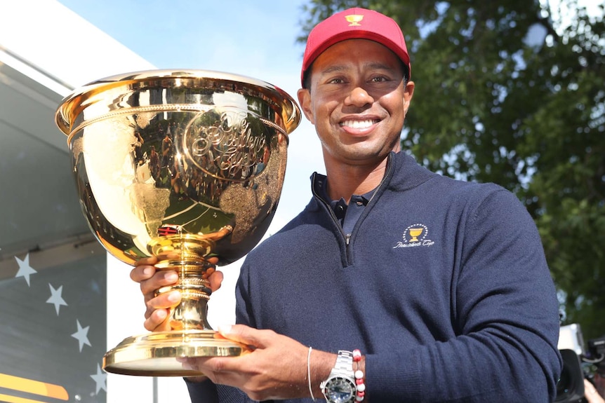 Man holding large gold trophy looks towards the camera.