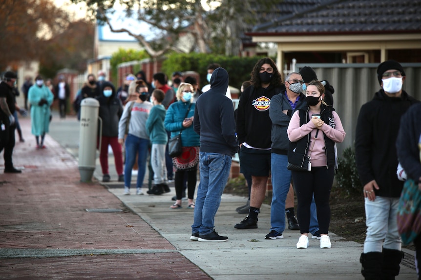 A queue of masked people standing on a pavement.