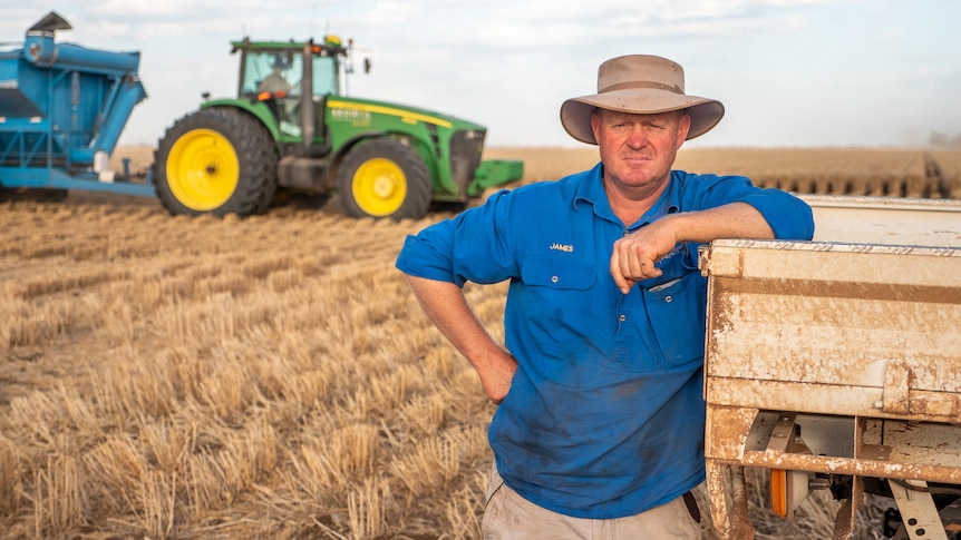 James Coggan leans on a utilty in a wheat paddock with a tractor behind him, Inglestone, southern Queensland October 2021.