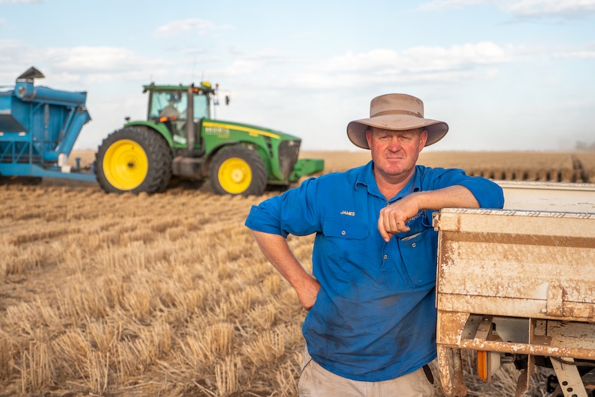 James Coggan leans on a utilty in a wheat paddock with a tractor behind him, Inglestone, southern Queensland October 2021.