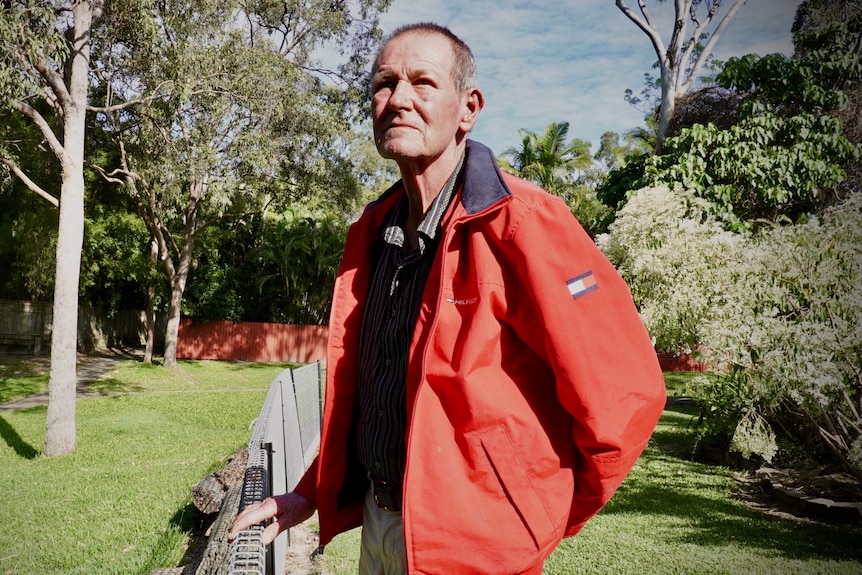 Greg Wheeldon stands in his backyard. He wears a red jacket.
